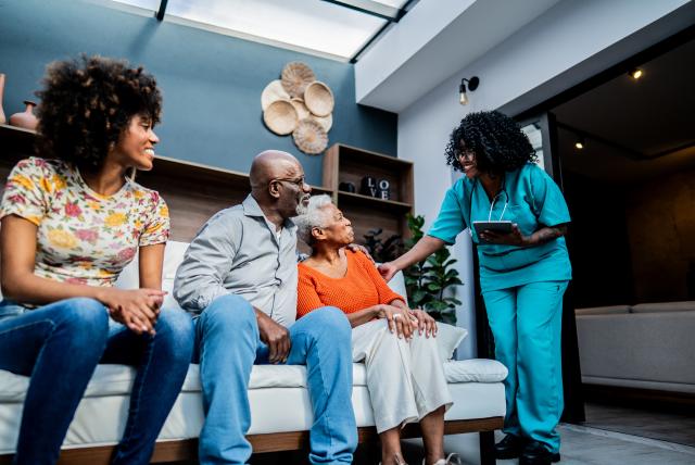A family with two older adults and an adult woman smile and talk with a nurse