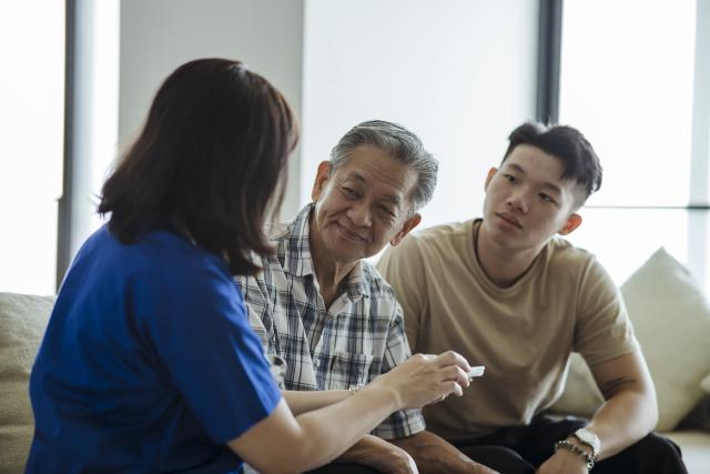 Older Asian man and his adult son talking to a nurse in their home