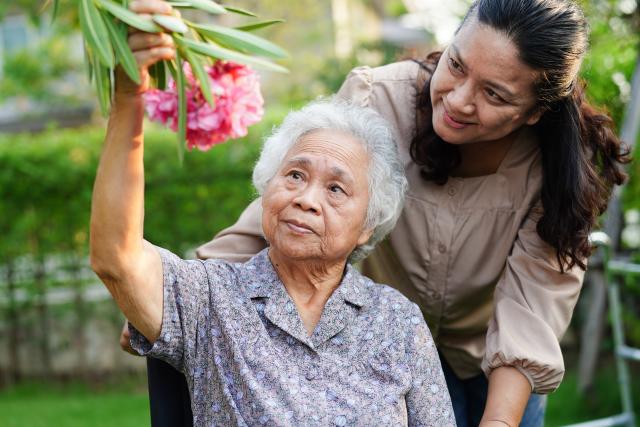 An adult woman pushing her mother around in a wheelchair, looking at flowers