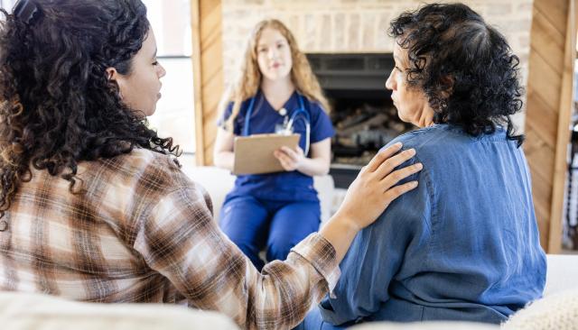 Woman comforting older woman while talking to a home nurse.