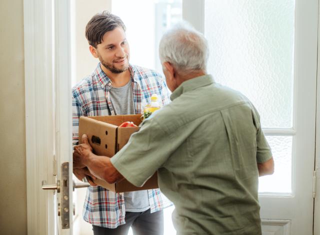 Adult man bringing groceries to his older adult neighbor
