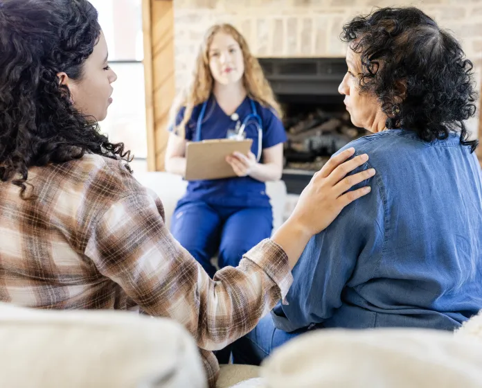 Woman comforting older woman while talking to a home nurse.