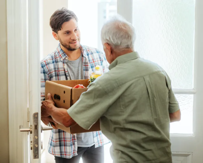 Adult man bringing groceries to his older adult neighbor